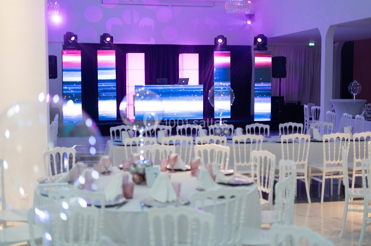 Salle de réception décorée avec des tables dressées et une scène équipée d'écrans lumineux et de lumières colorées.