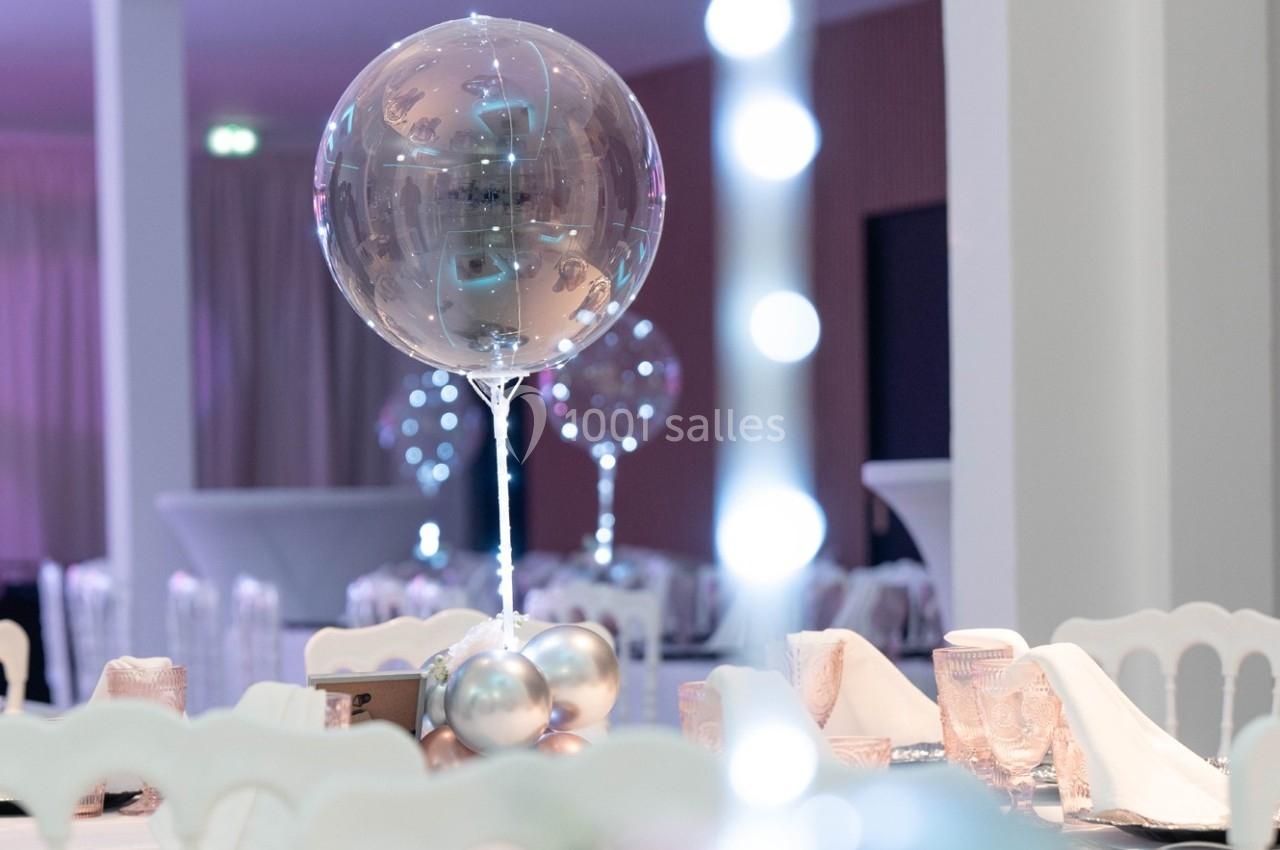 Ballon transparent décoratif avec des reflets métalliques, entouré de ballons argentés sur une table de réception élégante.
