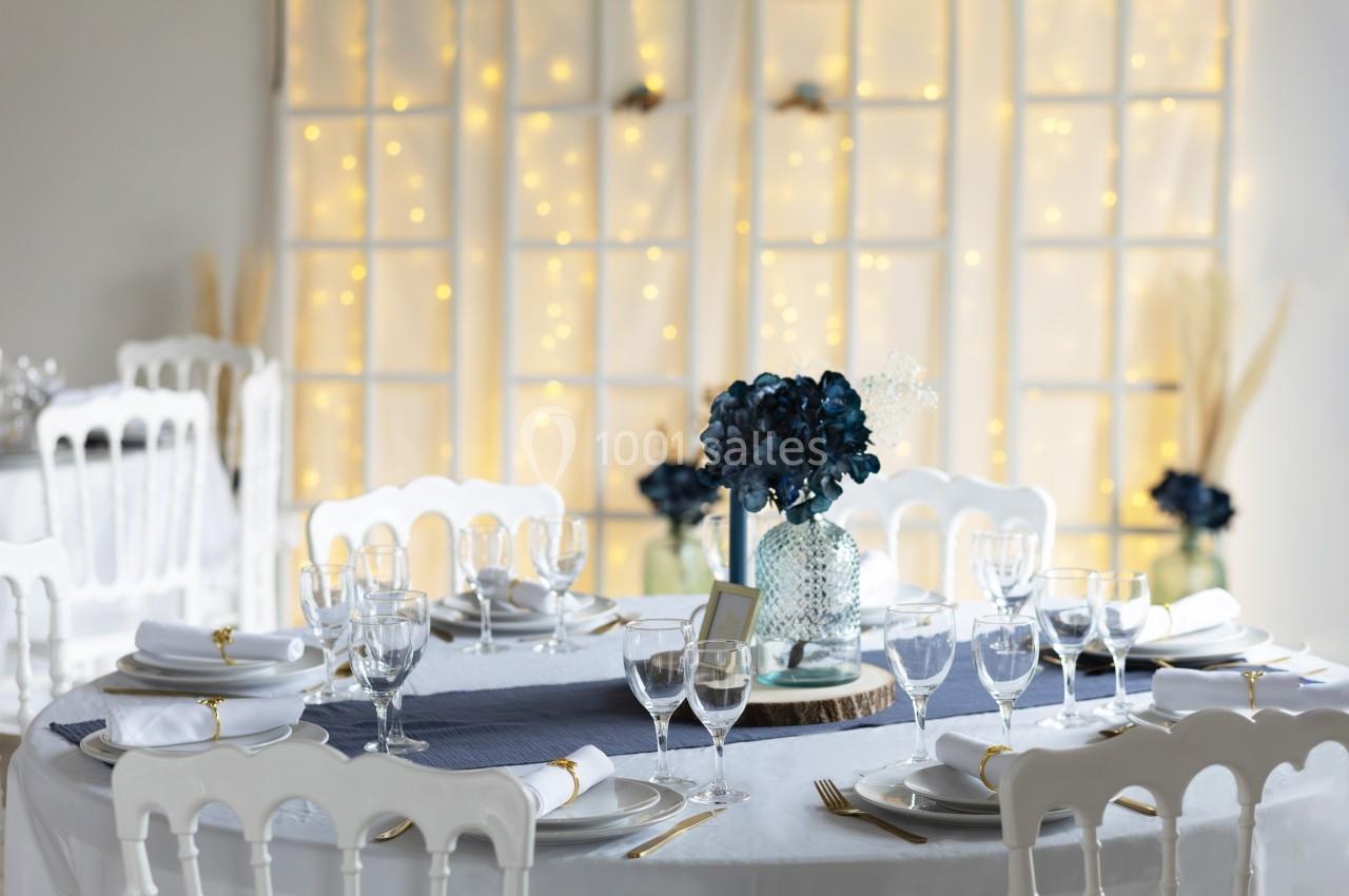 Table élégamment dressée avec vaisselle blanche, nappe blanche, chemin de table bleu et centre de table floral.