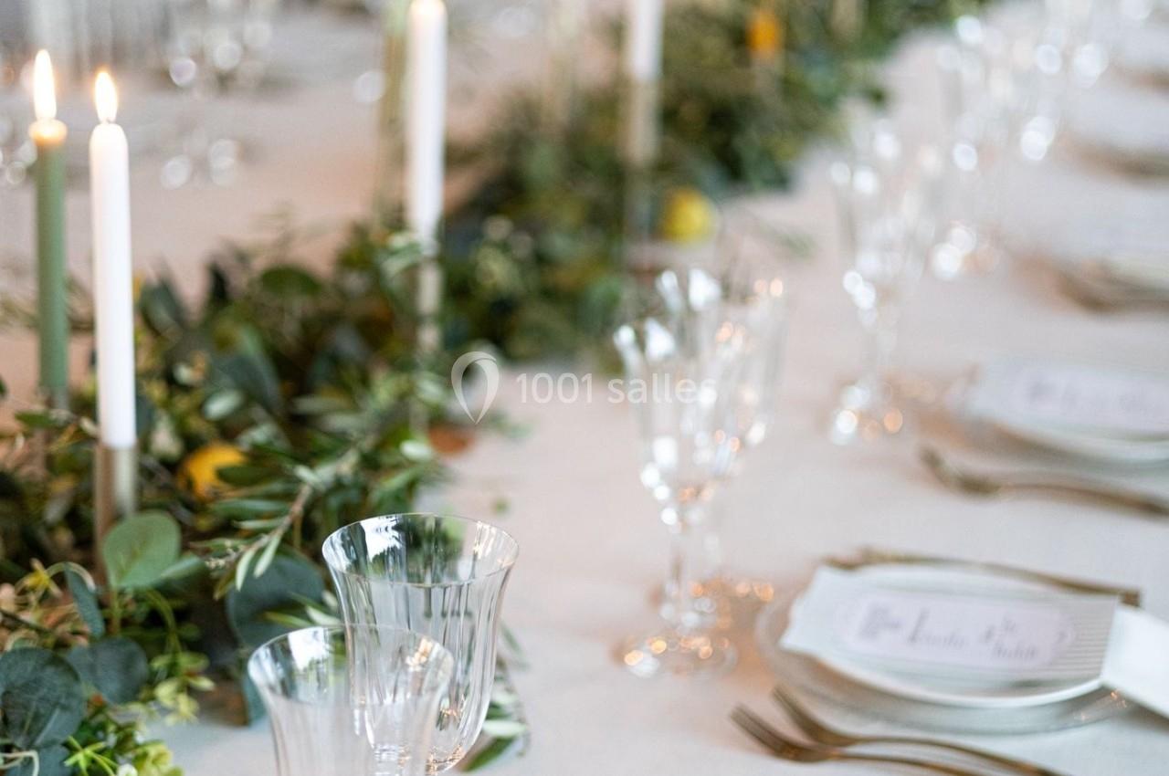 Table élégamment dressée avec des chandelles, des verres en cristal et une décoration végétale centrale.