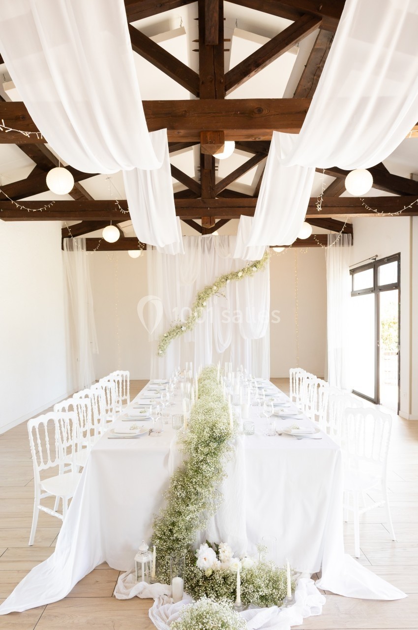 Salle de réception décorée avec des tables blanches, des chaises assorties et des drapés suspendus au plafond.