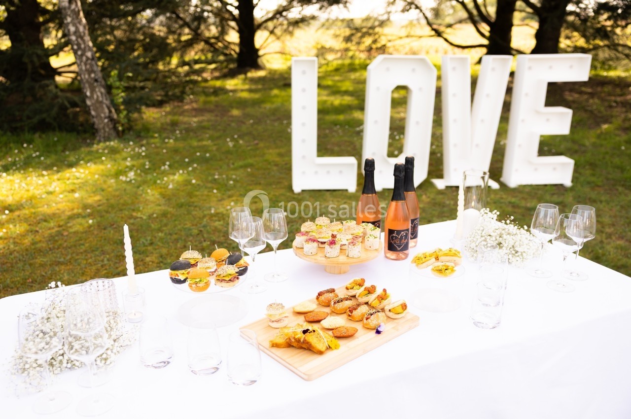 Table décorée en extérieur avec des amuse-bouches, des bouteilles de champagne et le mot ’LOVE’ en lettres lumineuses.