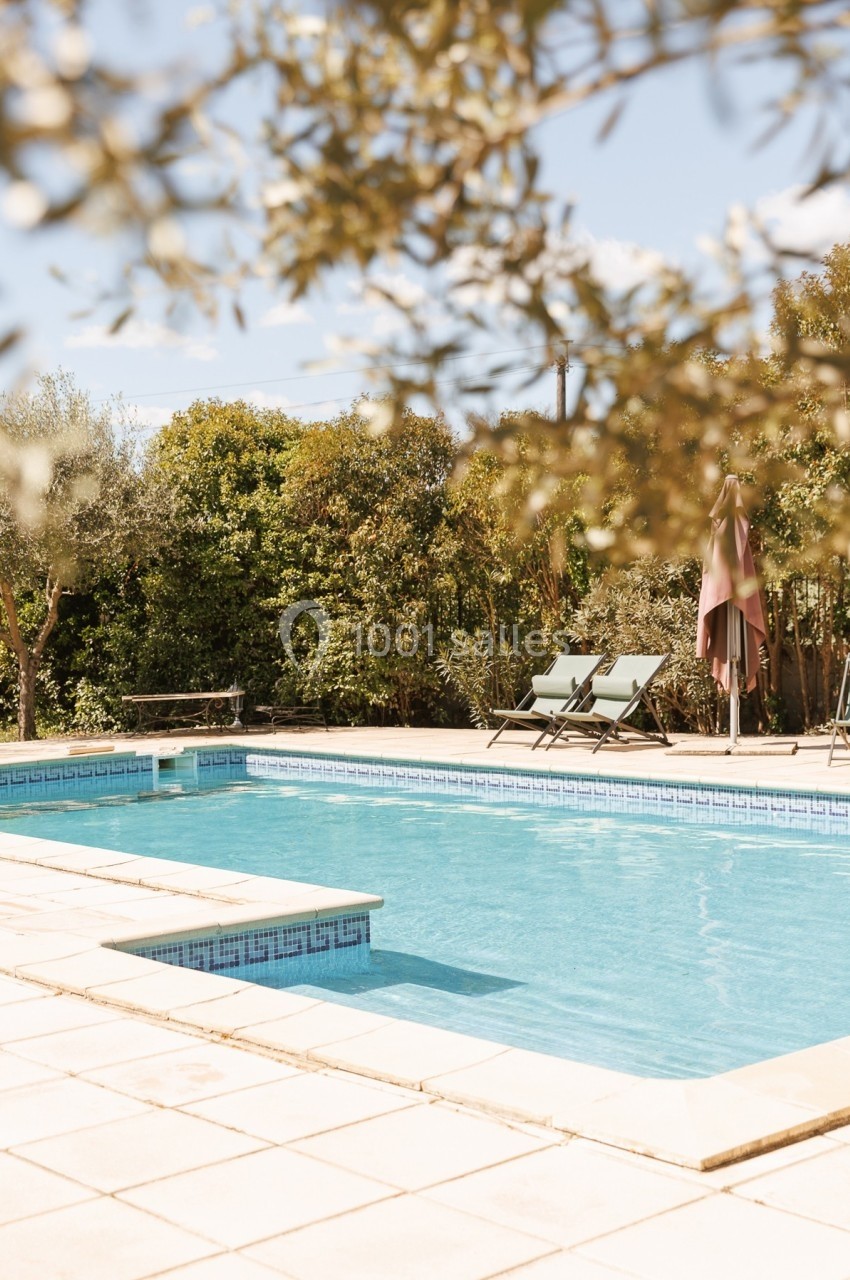 Piscine extérieure entourée de végétation, avec deux transats et un parasol sur une terrasse ensoleillée.