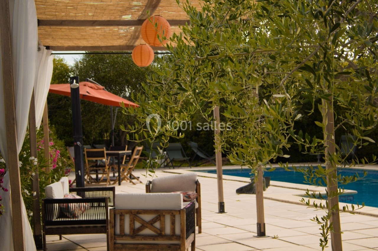 Terrasse ensoleillée avec mobilier en bois, piscine, parasol orange et olivier sous une pergola en bambou.