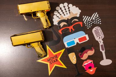 Miniature Accessoires festifs Accessoires de fête colorés sur une table en bois, incluant lunettes, moustaches, micro et pistolets dorés.