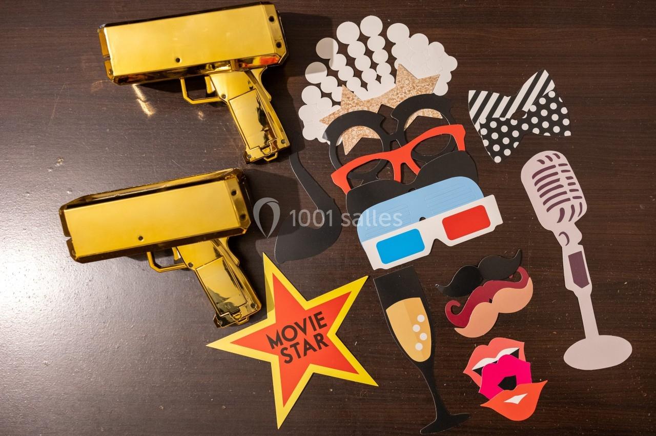 Accessoires de fête colorés sur une table en bois, incluant lunettes, moustaches, micro et pistolets dorés.