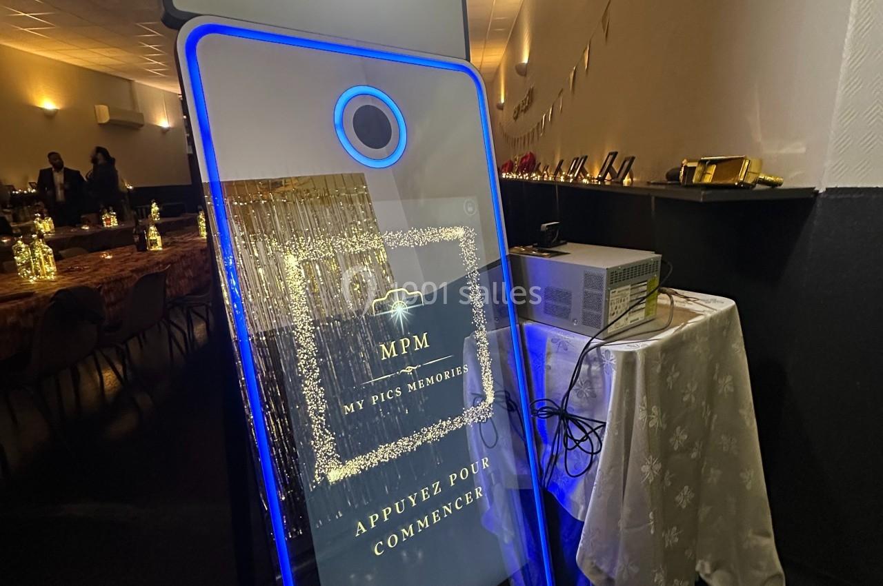 Borne photo interactive éclairée en bleu, installée dans une salle de réception avec des tables décorées en arrière-plan.