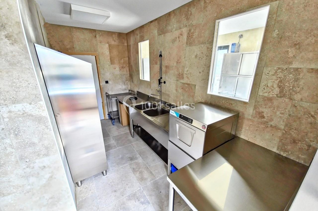 Cuisine professionnelle avec évier inox, lave-vaisselle, plan de travail en métal et murs en carrelage beige.