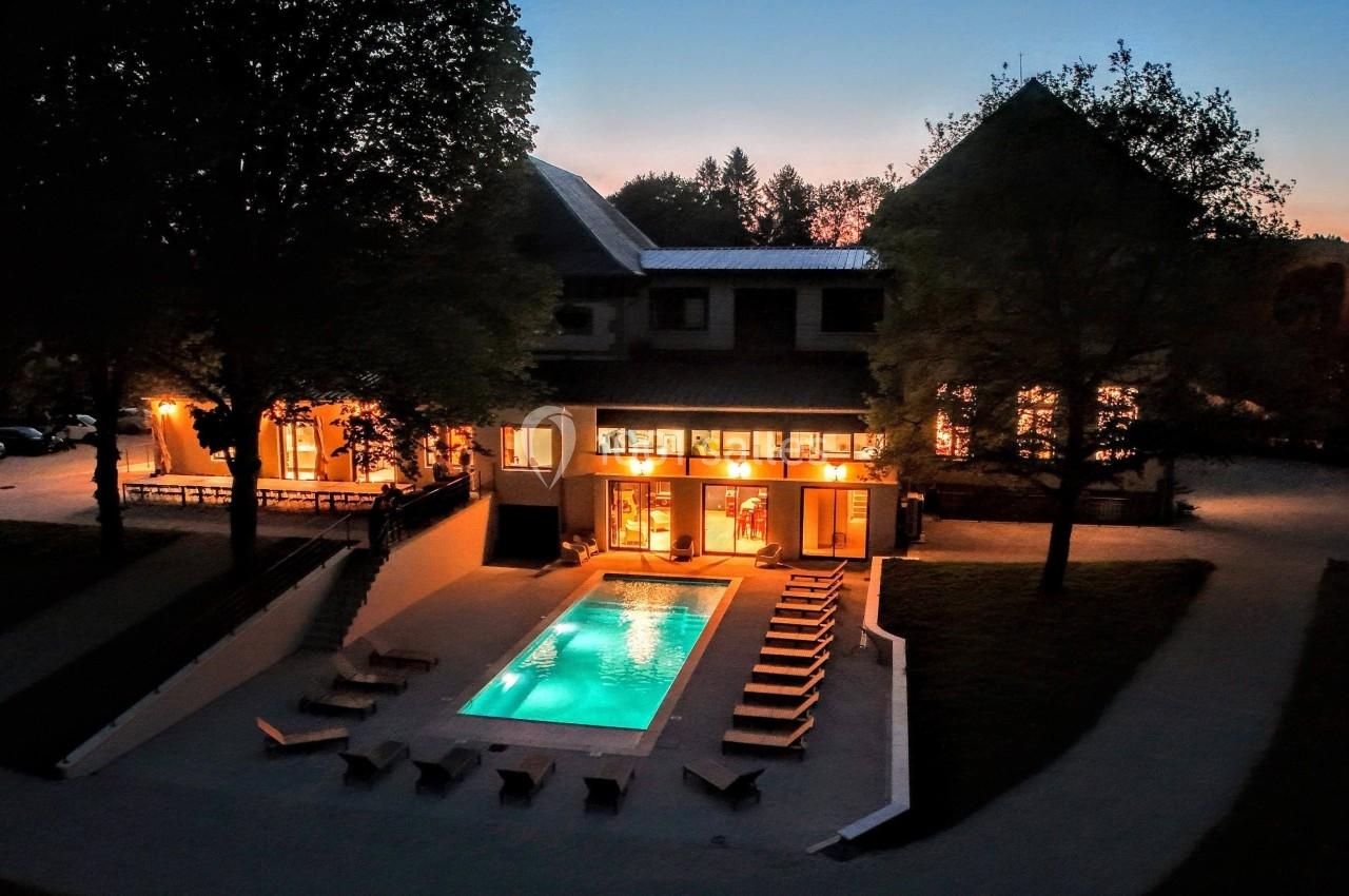 Vue nocturne d'un bâtiment éclairé avec une piscine extérieure entourée de chaises longues et d'arbres.