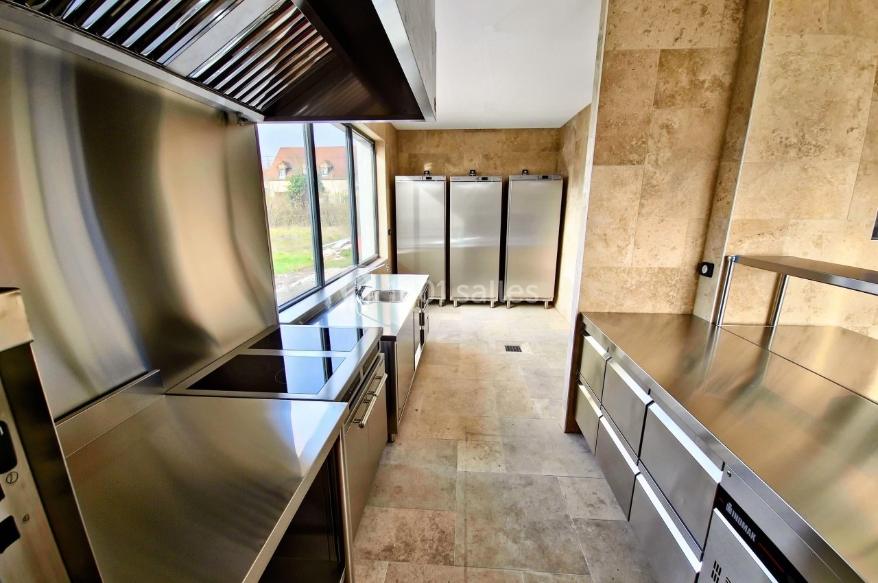 Cuisine professionnelle moderne avec équipements en acier inoxydable et murs en pierre beige.