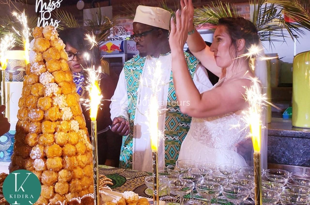 Une mariée et des invités devant une pièce montée éclairée par des cierges magiques lors d'une célébration.