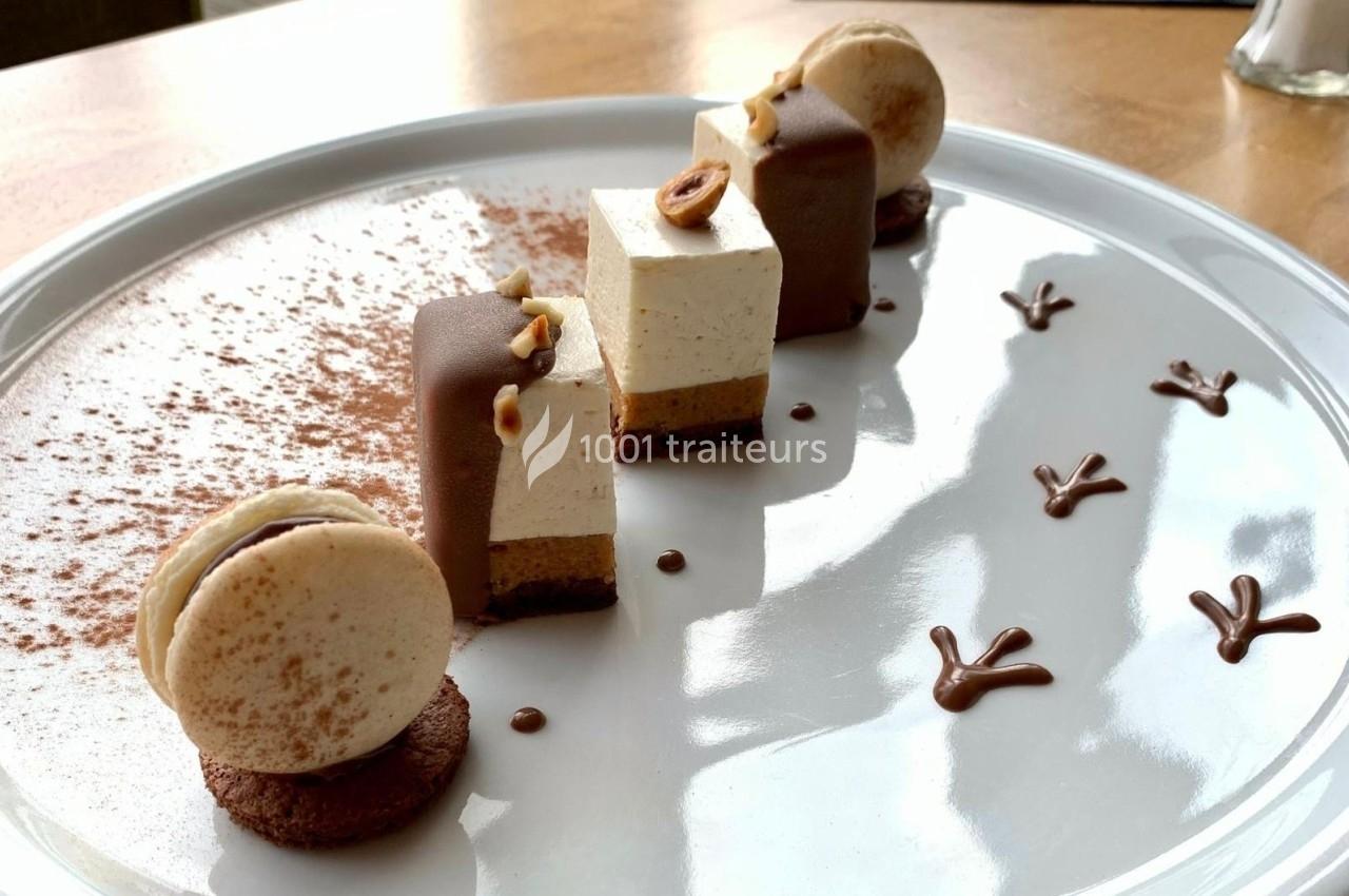 Dessert raffiné composé de mousses, macarons, chocolat et décorations en cacao sur une assiette blanche.