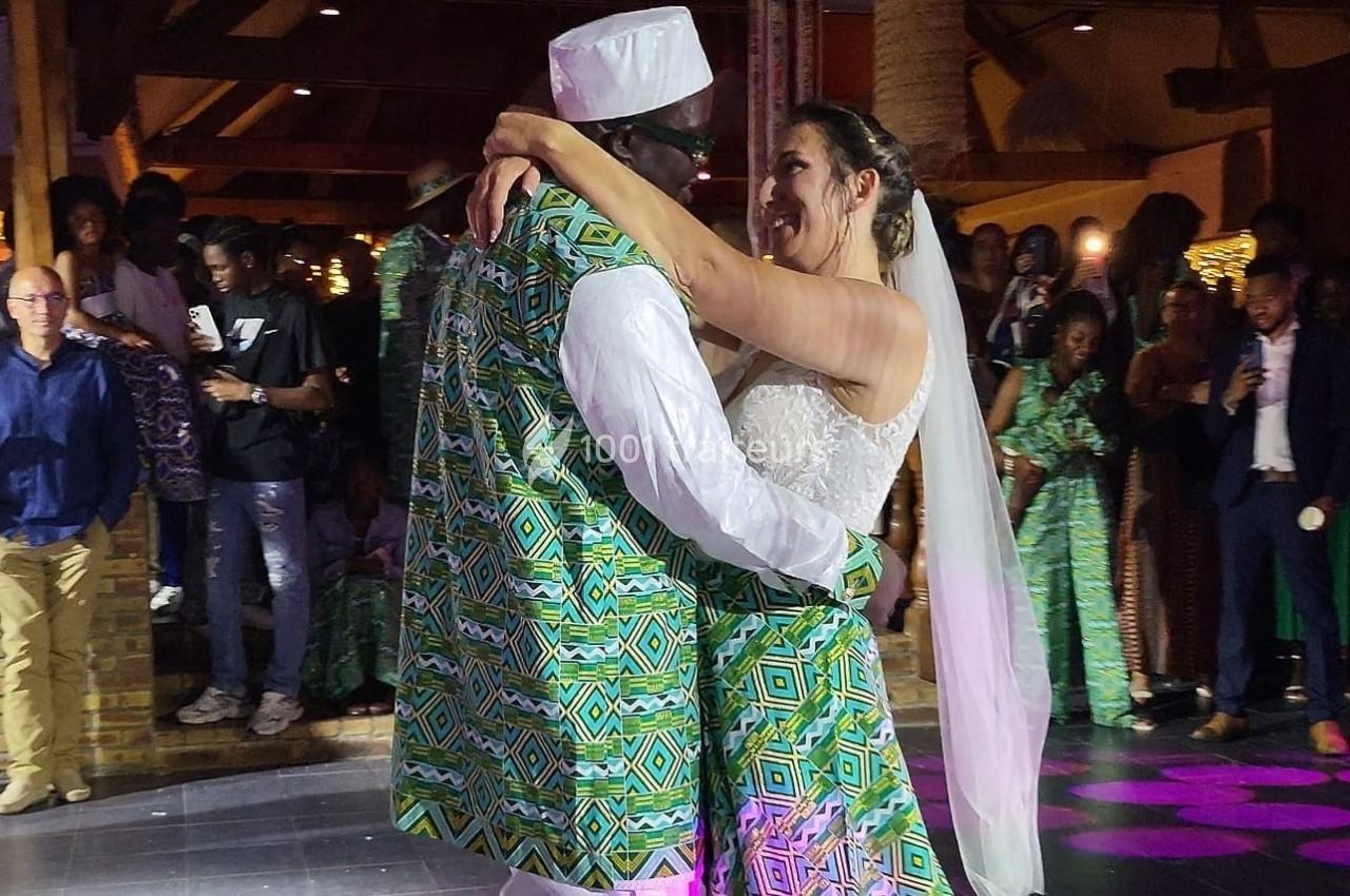 Un couple en tenue traditionnelle danse lors d'une célébration, entouré d'invités dans une salle éclairée.