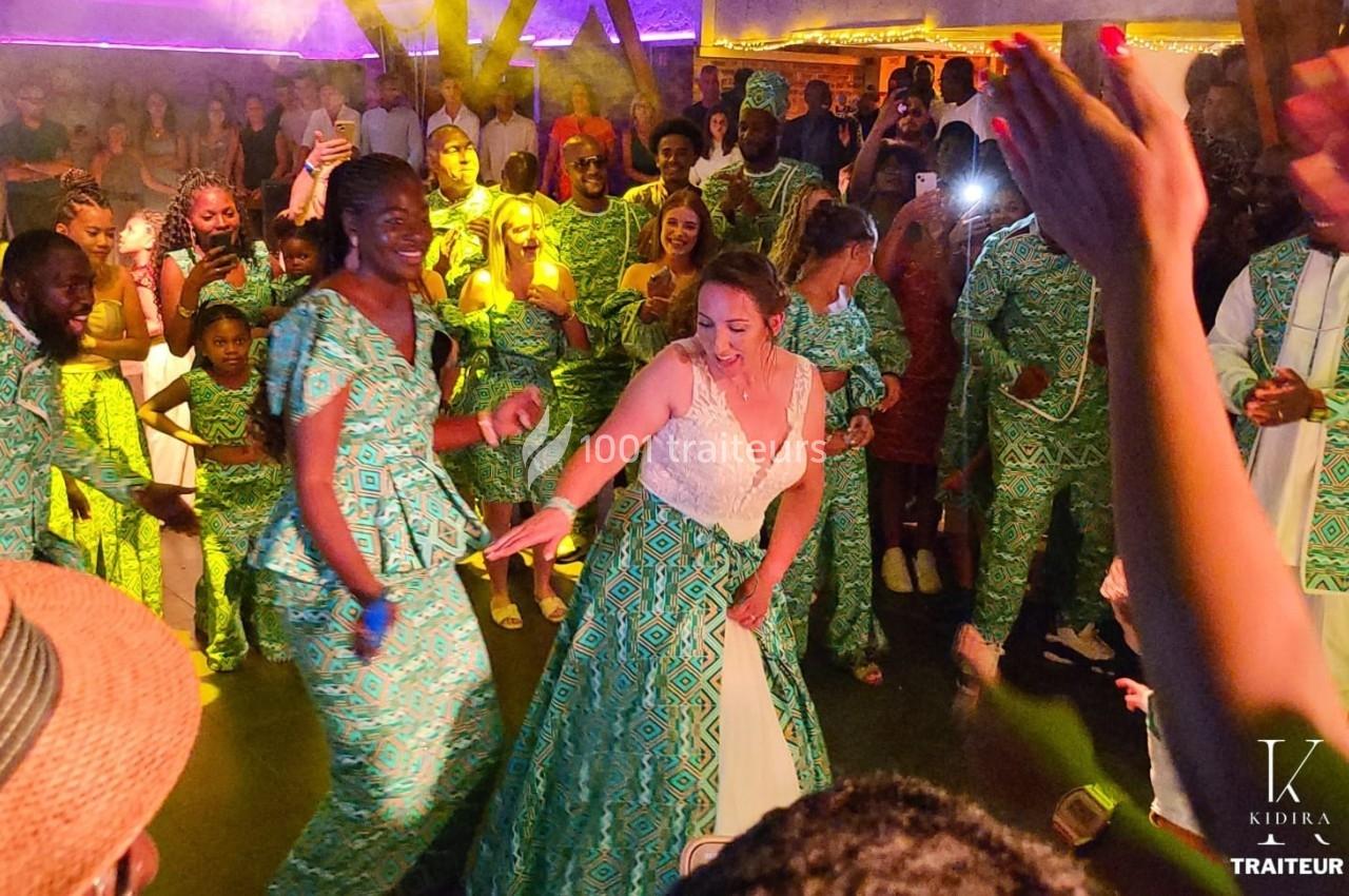 Des personnes dansent lors d'une fête, avec des tenues colorées et une ambiance festive éclairée.