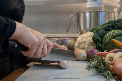 Une personne coupe un oignon sur une planche en bois, entourée de légumes frais et d'herbes aromatiques.