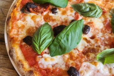 Une personne coupe un oignon sur une planche en bois, entourée de légumes frais et d'herbes aromatiques.
