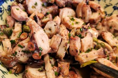 Une personne coupe un oignon sur une planche en bois, entourée de légumes frais et d'herbes aromatiques.