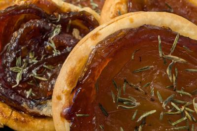 Une personne coupe un oignon sur une planche en bois, entourée de légumes frais et d'herbes aromatiques.