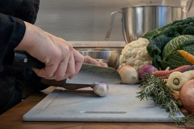 Une personne coupe un oignon sur une planche en bois, entourée de légumes frais et d'herbes aromatiques.