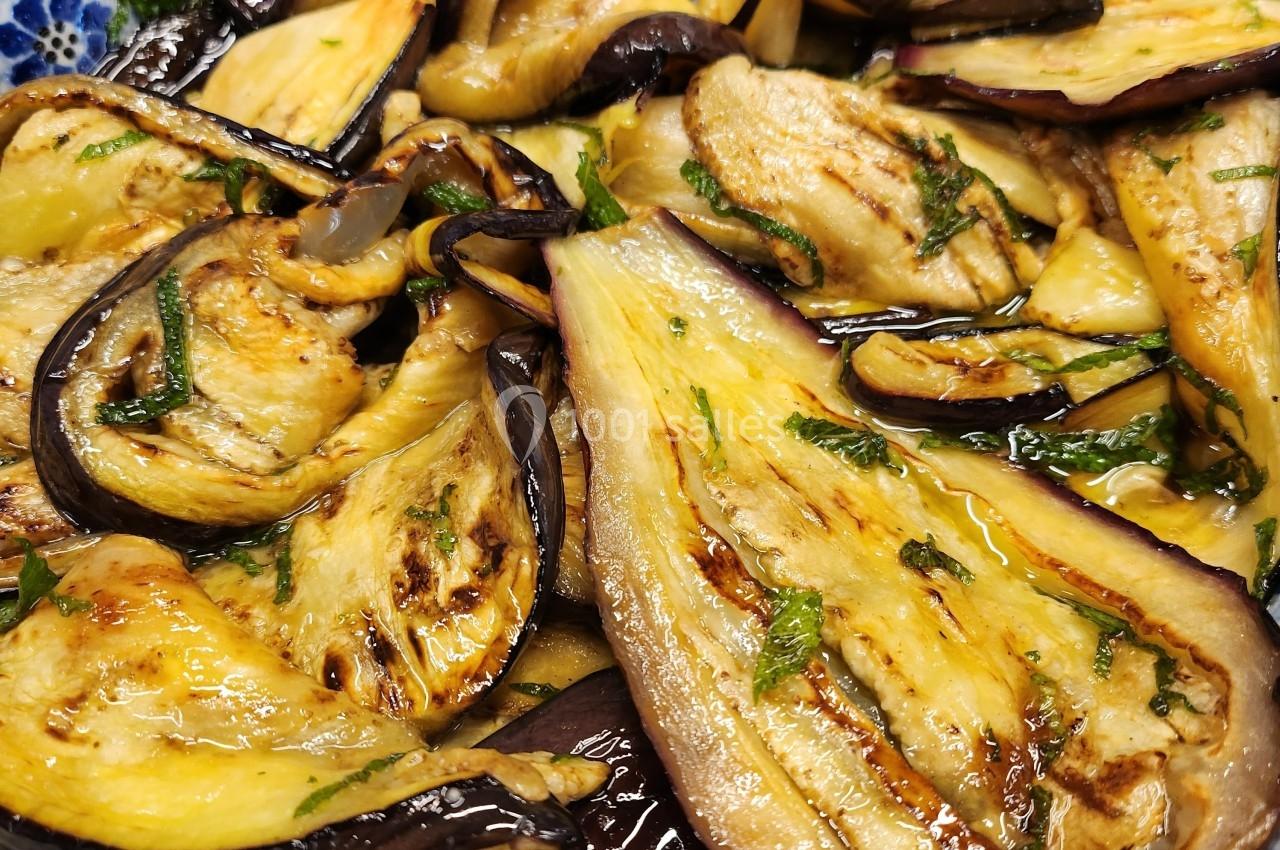 Tranches d'aubergines grillées assaisonnées avec des herbes fraîches, servies dans un plat à motifs bleus.