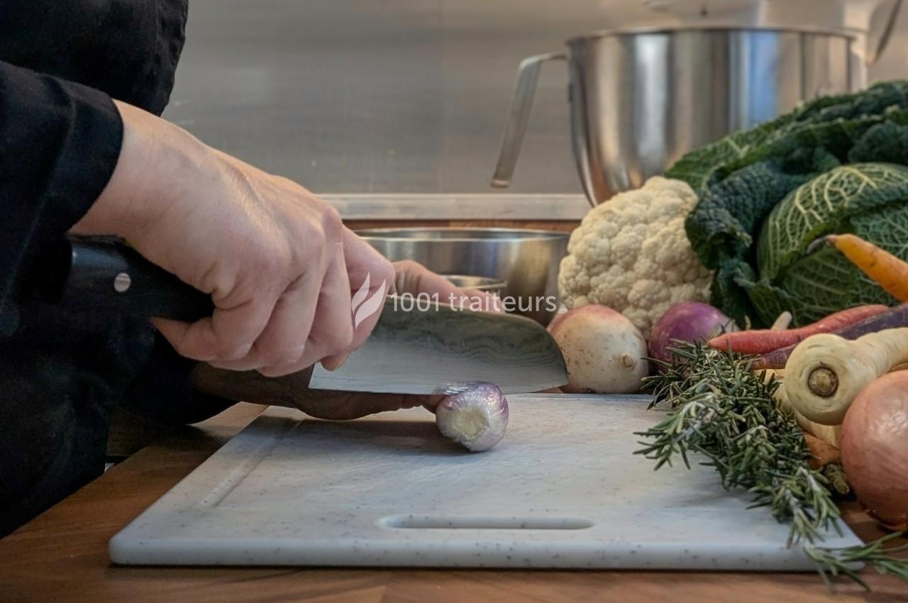 Une personne découpe un petit oignon sur une planche, entourée de légumes frais et d'herbes aromatiques.