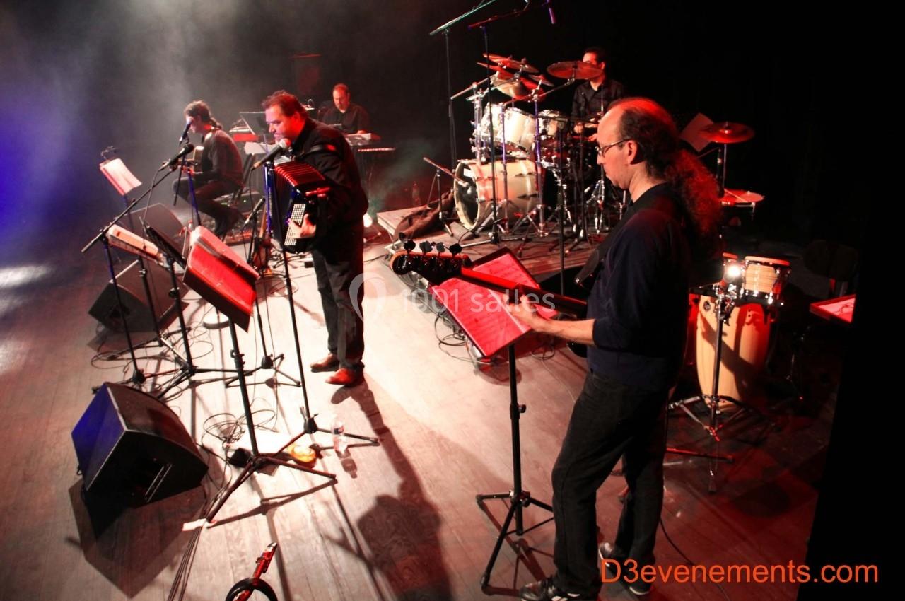 Un groupe de musiciens joue sur scène avec divers instruments, éclairé par des projecteurs.
