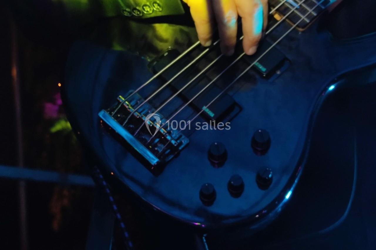 Gros plan sur une main jouant de la guitare basse noire sous des éclairages colorés lors d'un concert.