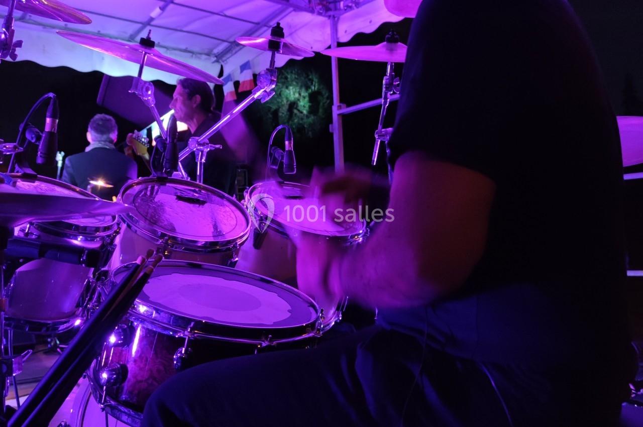 Un batteur joue sur une batterie sous une tente éclairée par des lumières violettes lors d'un concert en plein air.