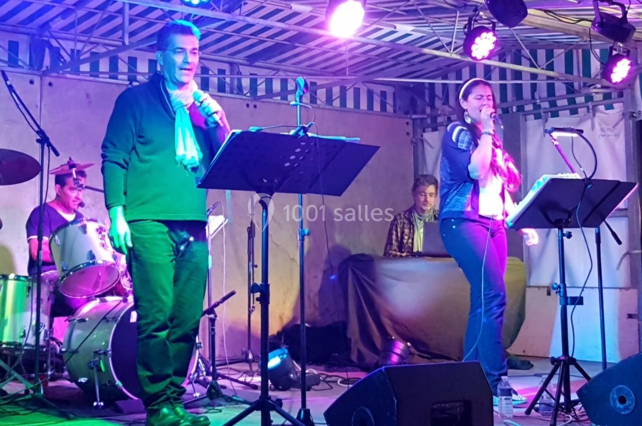 Deux chanteurs sur scène accompagnés d'un batteur et d'un claviériste, sous un éclairage coloré.