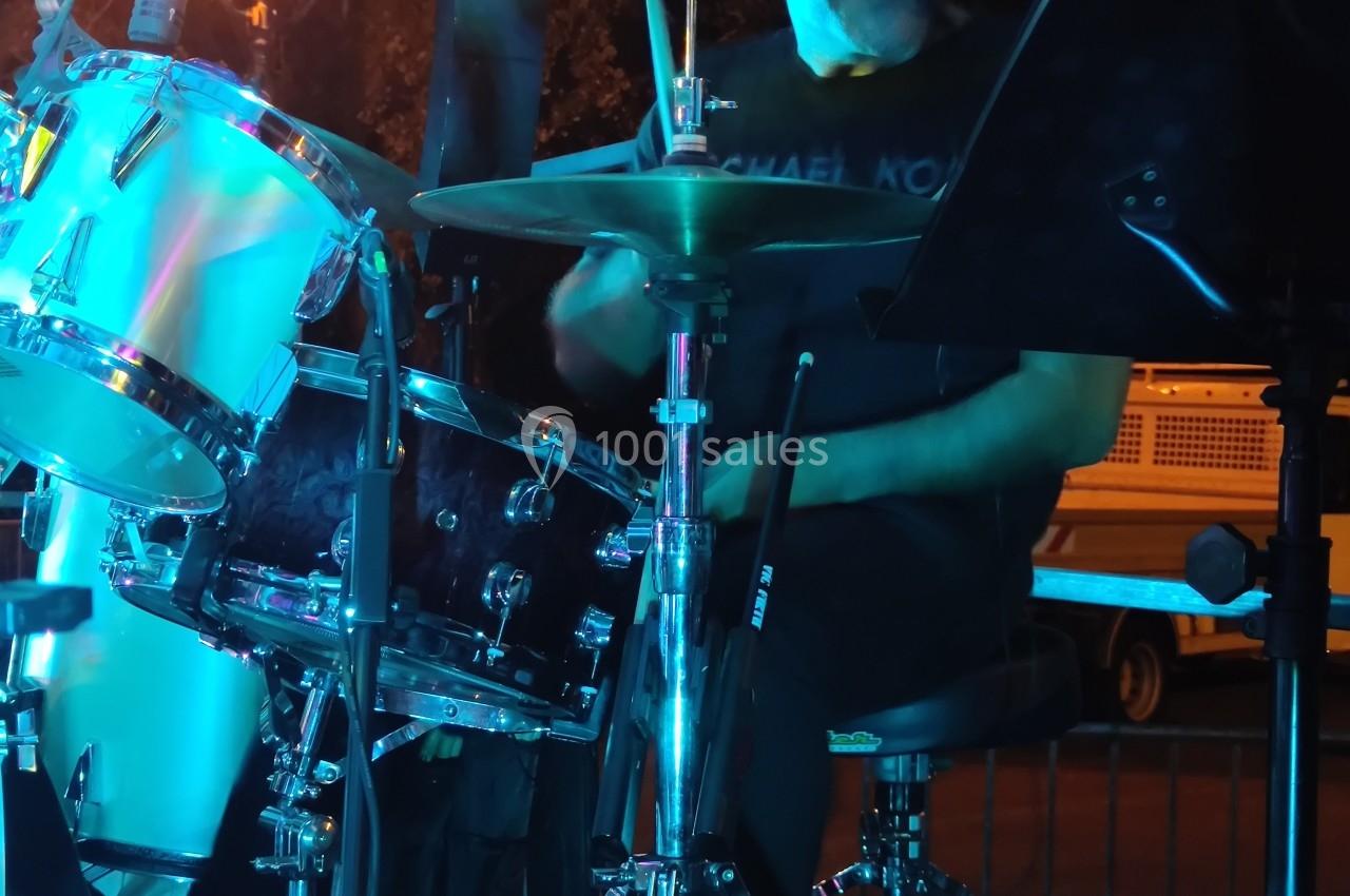 Un batteur joue sur une batterie sous un éclairage bleu, avec un lampadaire en arrière-plan.