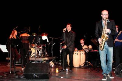 Un batteur joue sur une batterie argentée sur une scène sombre, avec un micro à proximité.