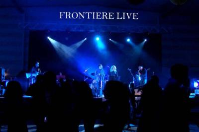 Un batteur joue sur une batterie argentée sur une scène sombre, avec un micro à proximité.