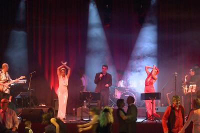 Un batteur joue sur une batterie argentée sur une scène sombre, avec un micro à proximité.