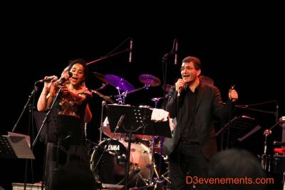 Un batteur joue sur une batterie argentée sur une scène sombre, avec un micro à proximité.