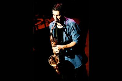 Un batteur joue sur une batterie argentée sur une scène sombre, avec un micro à proximité.