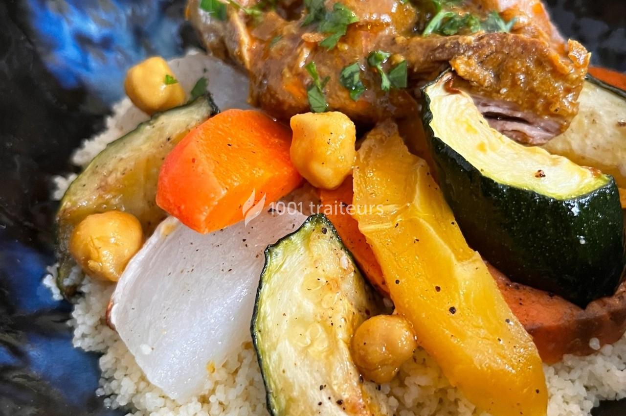 Plat de couscous garni de légumes colorés, pois chiches et viande en sauce, servi dans une assiette noire.