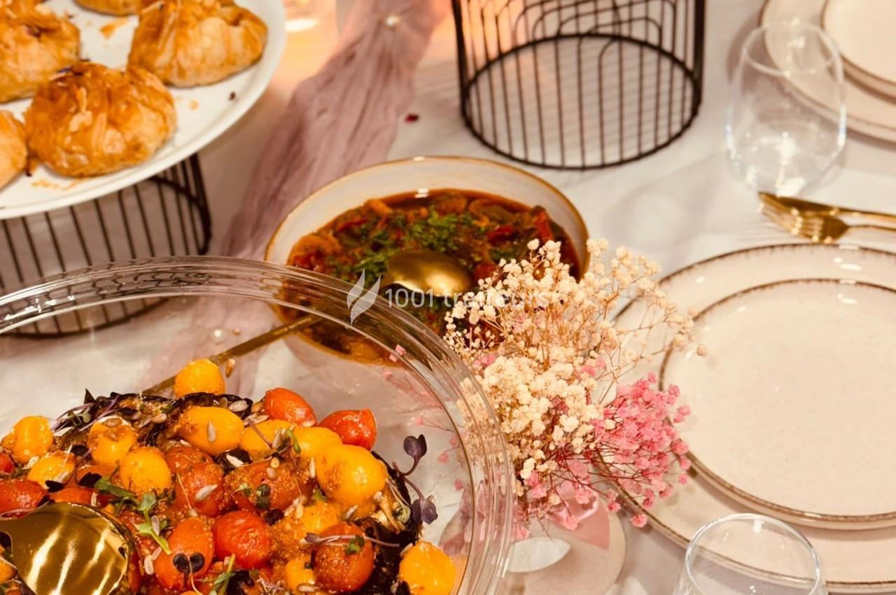 Assortiment de plats colorés sur une table dressée, comprenant une salade de tomates et des pâtisseries.