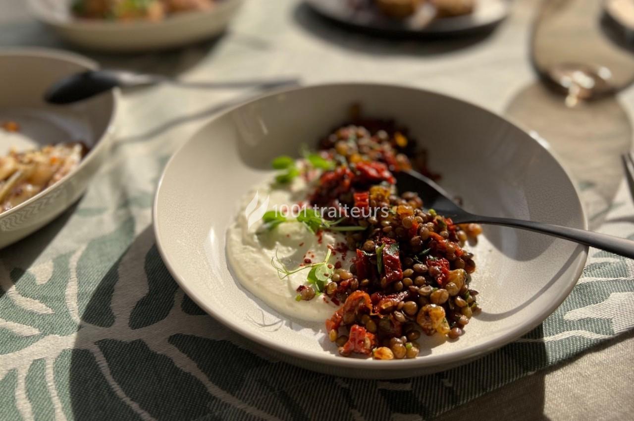 Assiette de lentilles garnies de légumes rôtis et herbes fraîches, accompagnée de sauce blanche, sur une table éclairée par…