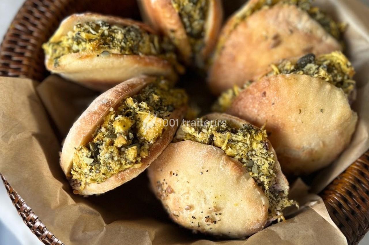 Pains garnis d'un mélange d'œufs brouillés et d'herbes, présentés dans un panier en osier tapissé de papier.