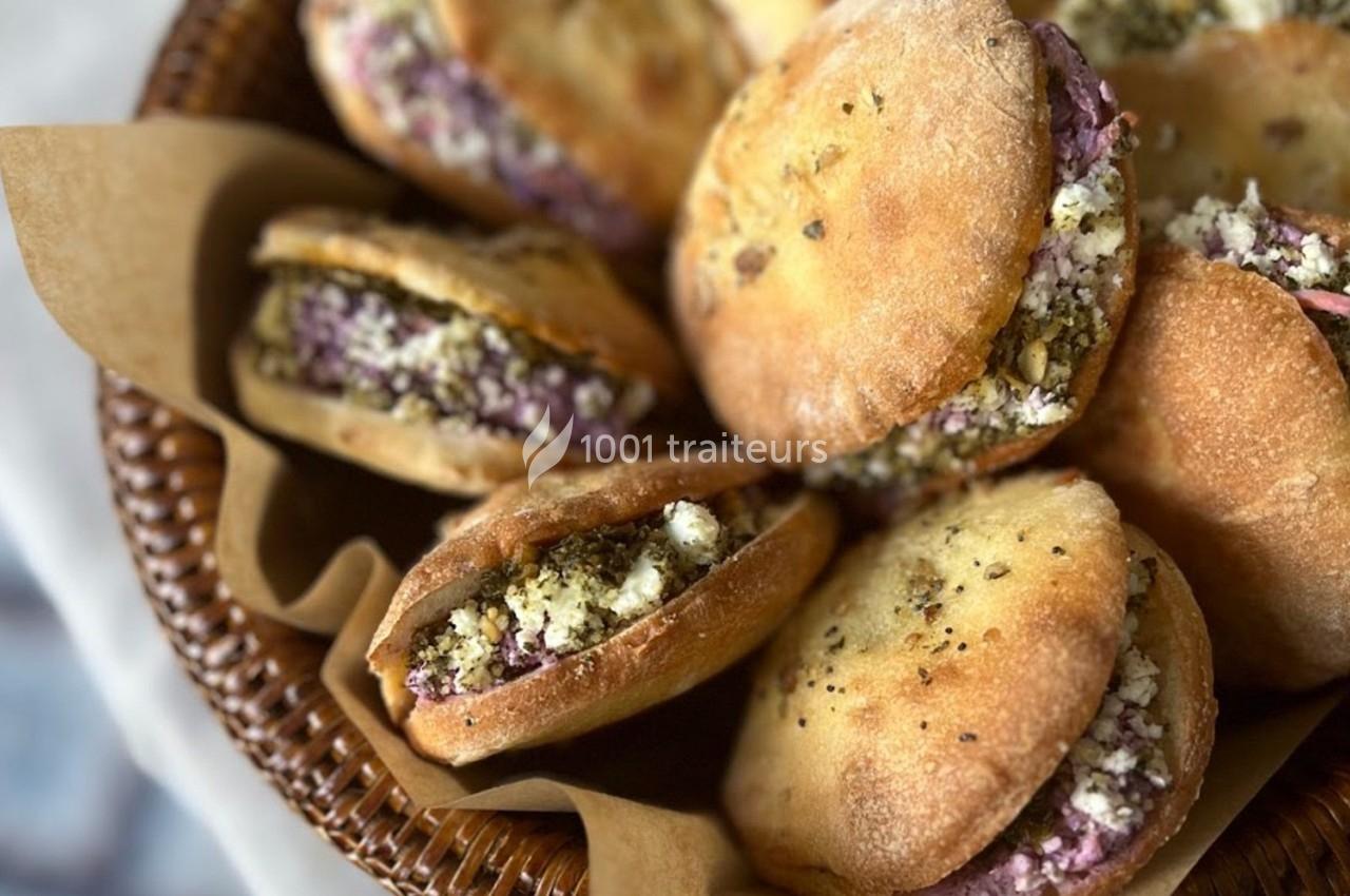 Pains garnis de fromage, épices et légumes, disposés dans un panier en osier avec du papier brun.