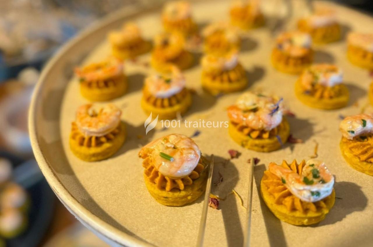 Plateau de bouchées apéritives garnies de crevettes et d'une base orangée, présenté sur un plat rond beige.