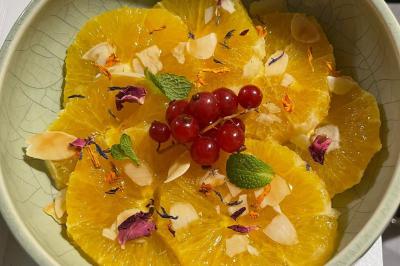 Tranches d'orange garnies de groseilles, pétales de fleurs, amandes effilées et feuilles de menthe dans une assiette.