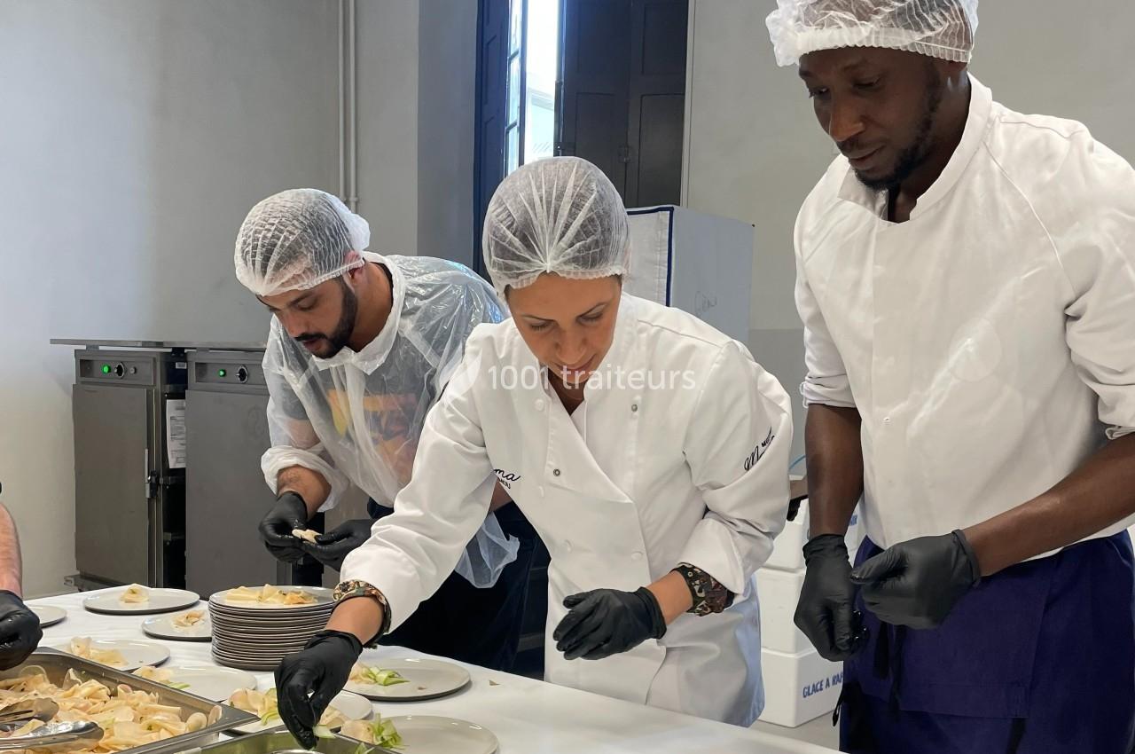 Trois cuisiniers préparent et dressent des assiettes dans une cuisine professionnelle.