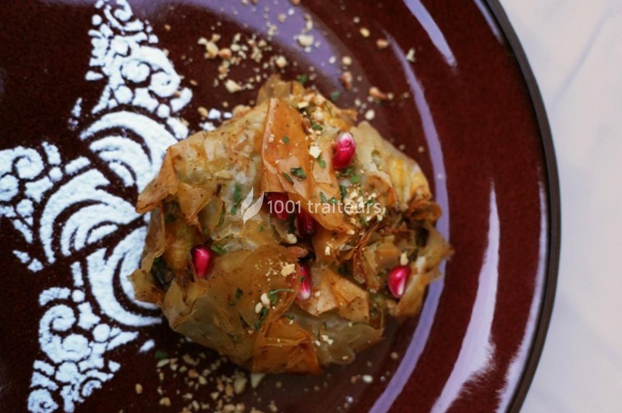 Feuilleté doré garni de graines de grenade, herbes fraîches et éclats de noix, présenté sur une assiette décorative.