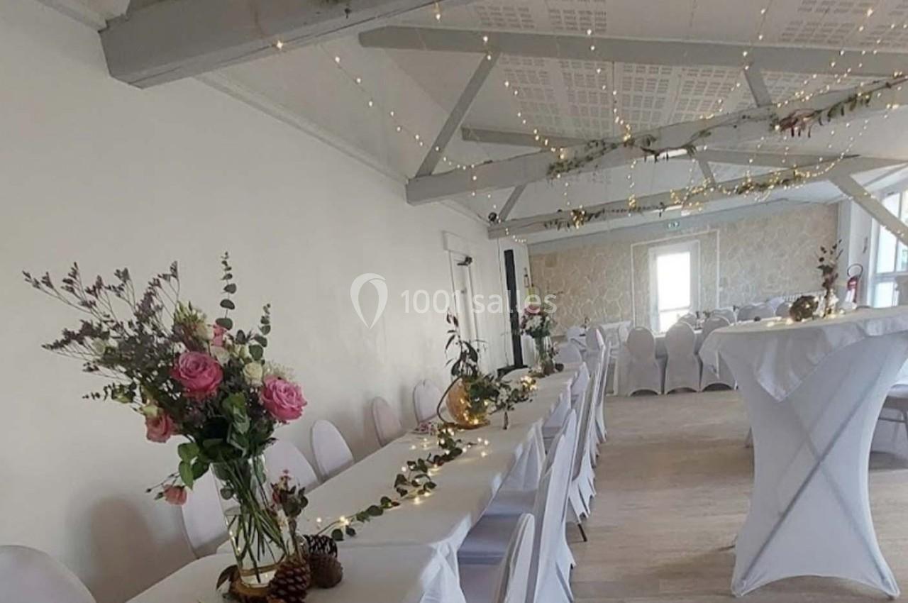 Salle de réception décorée avec des guirlandes lumineuses, des fleurs et des nappes blanches sur les tables.