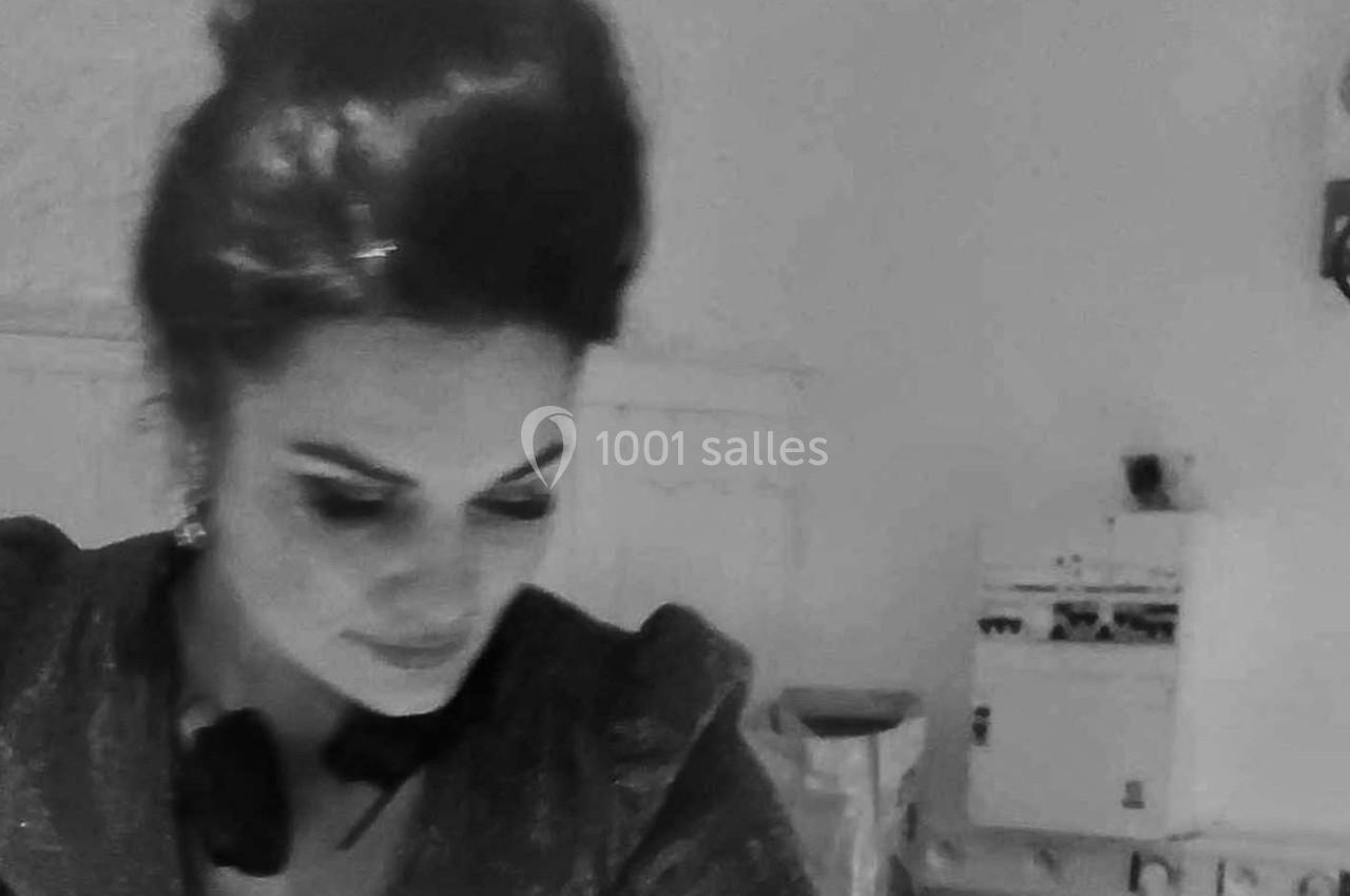 Femme aux cheveux relevés regardant vers le bas dans une pièce éclairée, avec des meubles en arrière-plan.