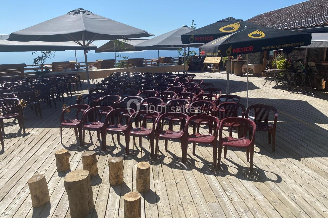 Terrasse en bois avec des chaises alignées sous des parasols, entourée de montagnes et d'un ciel dégagé.