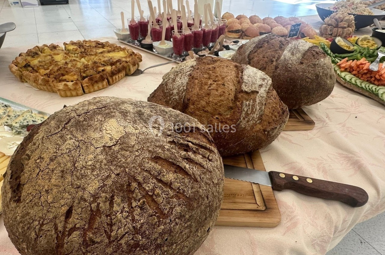 Trois pains rustiques sur une table garnie de plats variés, dont tartes, verrines et légumes.