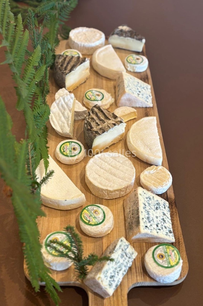 Plateau en bois garni de divers fromages, dont des fromages à pâte molle et persillée, décoré de branches de fougère.