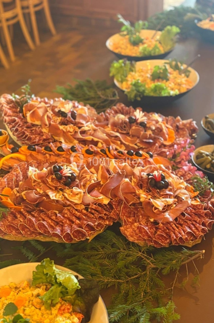 Plateau de charcuterie décoré avec des tranches de jambon et saucisson, entouré de salades et garnitures variées.